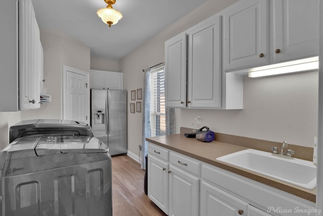 clothes washing area with sink, light hardwood / wood-style flooring, washing machine and dryer, and cabinets