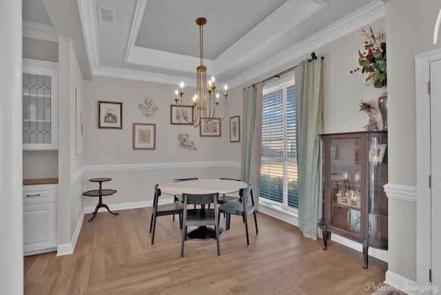 dining area featuring crown molding, a notable chandelier, light hardwood / wood-style floors, and a tray ceiling