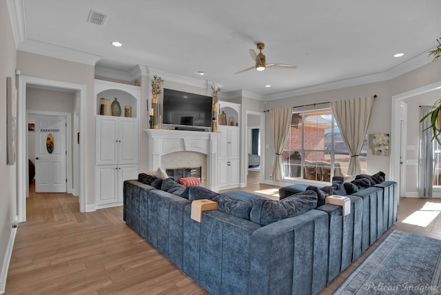 living room featuring crown molding, built in shelves, ceiling fan, and light wood-type flooring