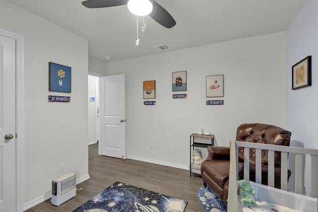 bedroom featuring ceiling fan, dark hardwood / wood-style flooring, and a crib