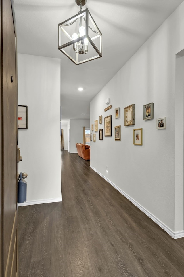 corridor with dark wood-type flooring and a chandelier