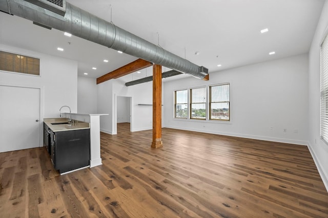 unfurnished living room featuring beam ceiling, dark hardwood / wood-style flooring, and sink