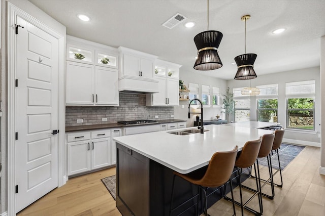 kitchen with sink, hanging light fixtures, white cabinets, and a kitchen island with sink