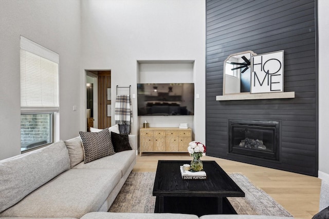 living room featuring wood finished floors, a towering ceiling, and a large fireplace