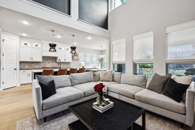 living room featuring light wood-type flooring, a towering ceiling, and sink