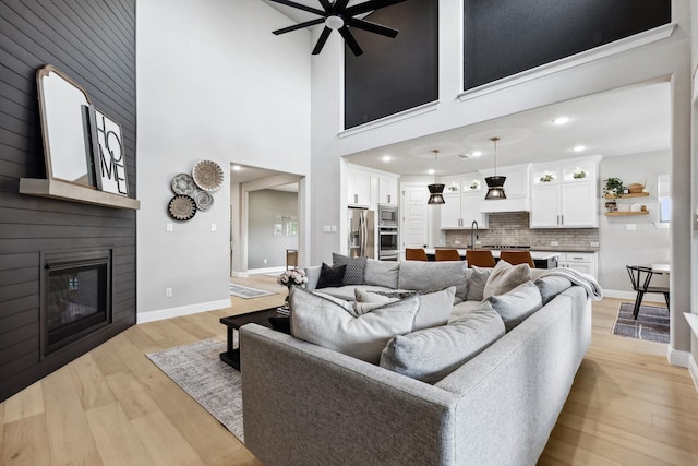 living room with light hardwood / wood-style floors, a fireplace, sink, a high ceiling, and ceiling fan