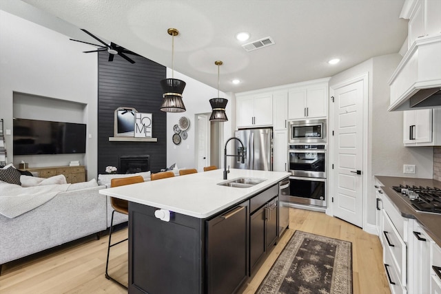 kitchen featuring stainless steel appliances, a large fireplace, hanging light fixtures, ceiling fan, and a center island with sink