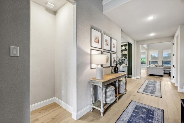 hallway with baseboards, a textured wall, recessed lighting, and light wood-style floors