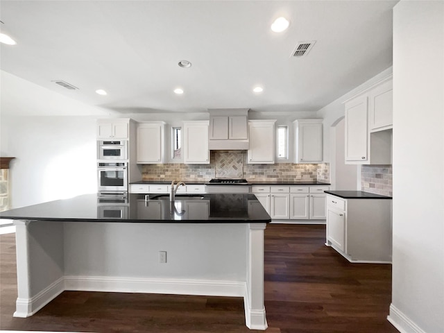 kitchen featuring appliances with stainless steel finishes, dark hardwood / wood-style flooring, an island with sink, and white cabinets