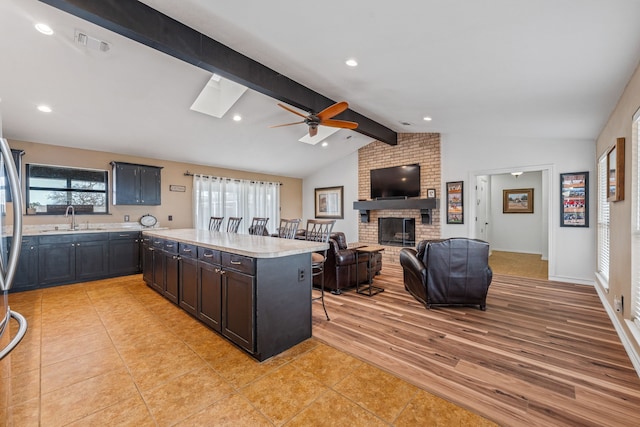 kitchen with sink, a brick fireplace, vaulted ceiling with skylight, a kitchen island, and light tile patterned flooring