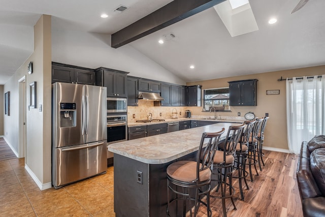 kitchen featuring a kitchen breakfast bar, vaulted ceiling with skylight, stainless steel appliances, sink, and a center island