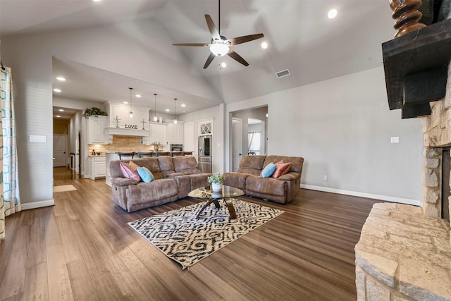 living room with a stone fireplace, ceiling fan, dark hardwood / wood-style flooring, and high vaulted ceiling