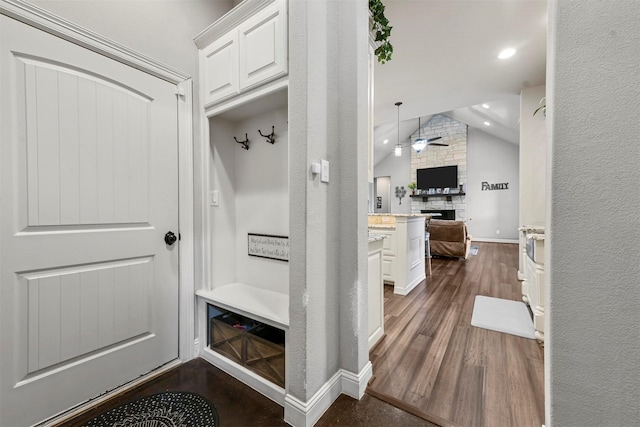 mudroom with dark hardwood / wood-style flooring, vaulted ceiling, ceiling fan, and a stone fireplace