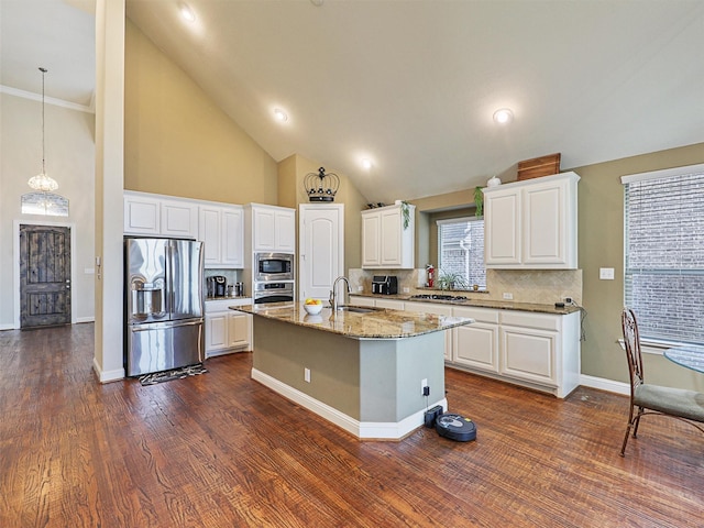 kitchen with appliances with stainless steel finishes, white cabinets, light stone countertops, an island with sink, and decorative backsplash