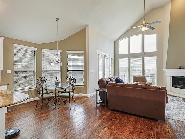 living room with plenty of natural light, ceiling fan with notable chandelier, dark wood-type flooring, and vaulted ceiling