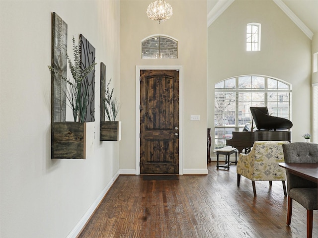 entrance foyer featuring high vaulted ceiling, dark hardwood / wood-style flooring, ornamental molding, and a notable chandelier