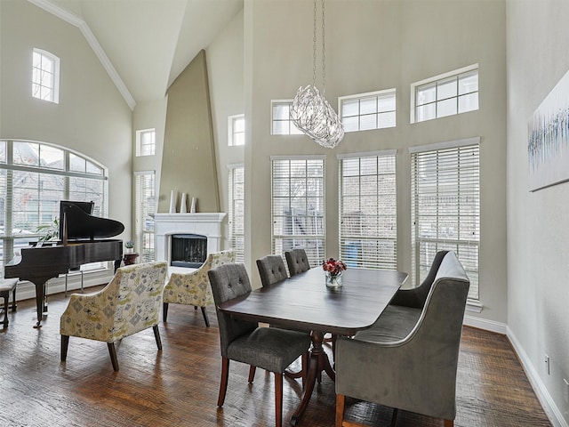 dining room with a large fireplace, a towering ceiling, crown molding, and dark hardwood / wood-style flooring