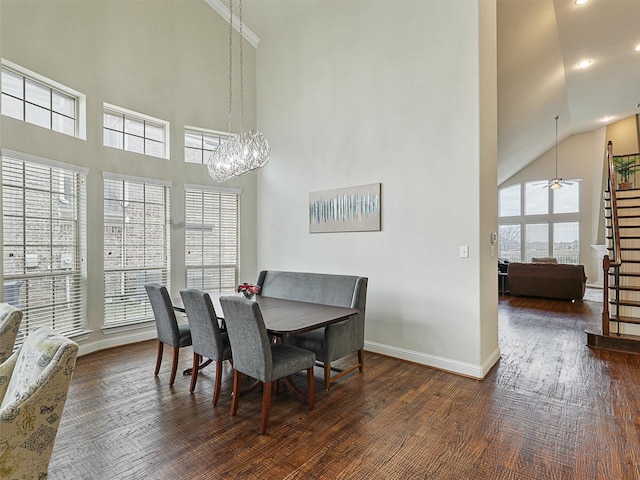 dining space with dark wood-type flooring, ceiling fan with notable chandelier, and a high ceiling