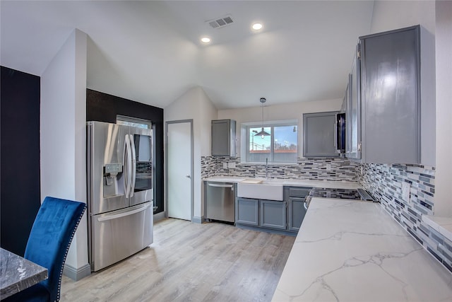 kitchen with gray cabinetry, light stone counters, tasteful backsplash, hanging light fixtures, and appliances with stainless steel finishes