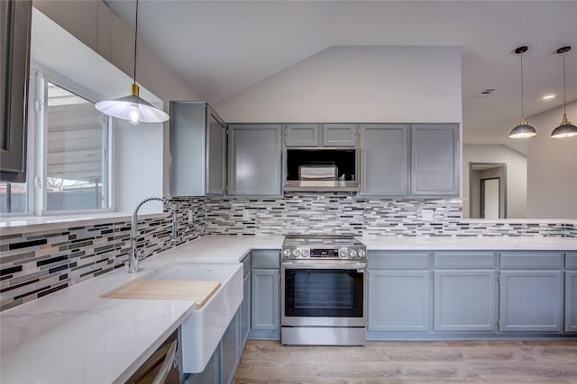 kitchen featuring stainless steel appliances, lofted ceiling, light stone counters, and decorative light fixtures