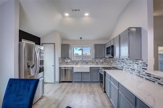 kitchen featuring vaulted ceiling, appliances with stainless steel finishes, sink, gray cabinetry, and hanging light fixtures