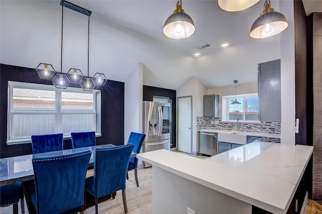 kitchen with hanging light fixtures, appliances with stainless steel finishes, decorative backsplash, and kitchen peninsula