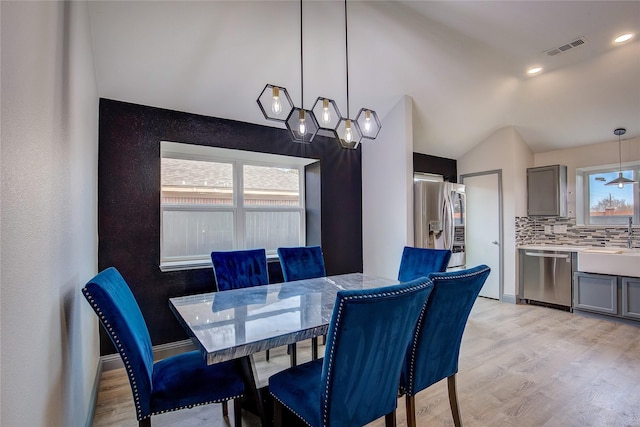 dining area with lofted ceiling, sink, and light wood-type flooring