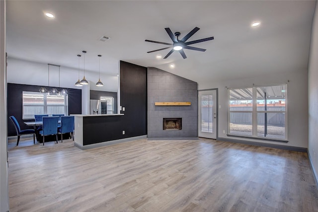 living room featuring a healthy amount of sunlight, a tiled fireplace, vaulted ceiling, and light wood-type flooring