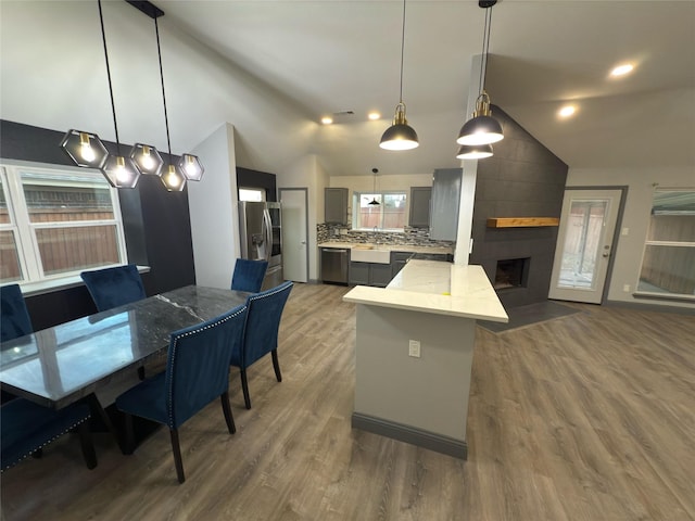 kitchen featuring appliances with stainless steel finishes, tasteful backsplash, hardwood / wood-style flooring, decorative light fixtures, and lofted ceiling