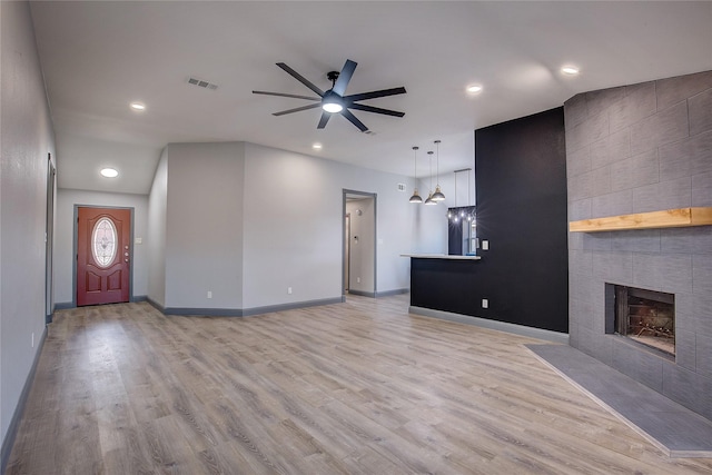 unfurnished living room with light hardwood / wood-style flooring, a tile fireplace, and ceiling fan