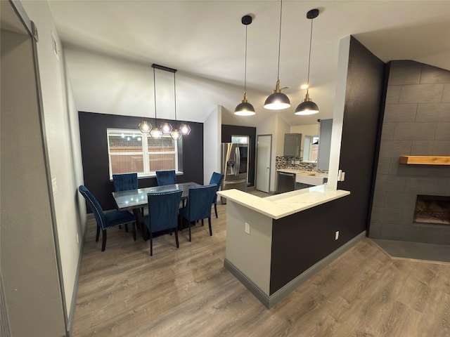 kitchen with vaulted ceiling, a fireplace, tasteful backsplash, kitchen peninsula, and stainless steel refrigerator