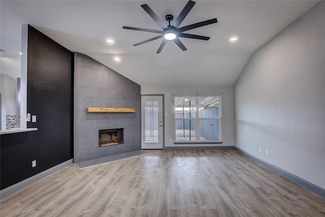 unfurnished living room featuring lofted ceiling, a tile fireplace, ceiling fan, and light wood-type flooring