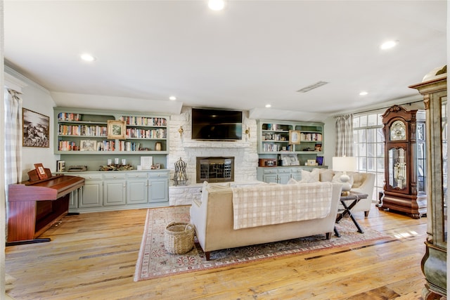 living room featuring built in shelves, a stone fireplace, and light wood-type flooring