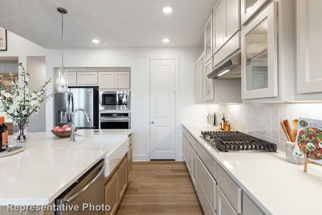 kitchen with sink, pendant lighting, stainless steel appliances, range hood, and light hardwood / wood-style floors