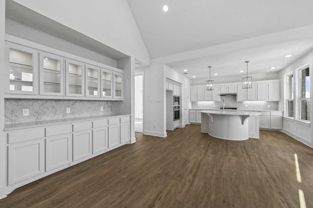 kitchen with dark wood-type flooring, a kitchen bar, decorative light fixtures, an island with sink, and white cabinets