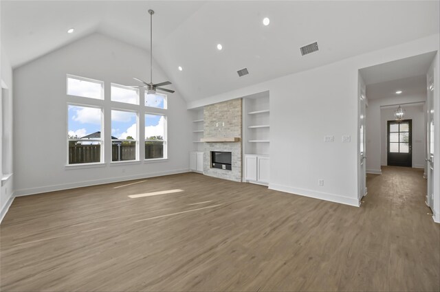 unfurnished living room with ceiling fan, wood-type flooring, a stone fireplace, and built in features