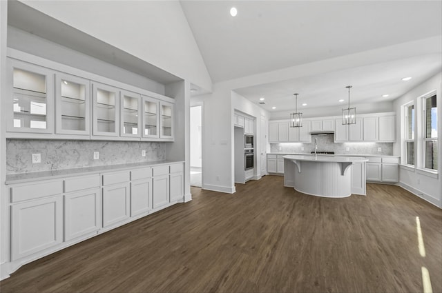 kitchen with a breakfast bar, dark hardwood / wood-style floors, an island with sink, pendant lighting, and white cabinets