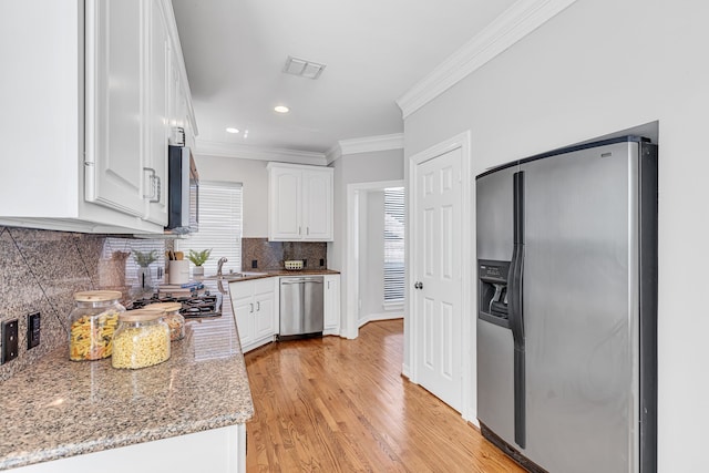 kitchen featuring backsplash, white cabinets, ornamental molding, appliances with stainless steel finishes, and light stone counters