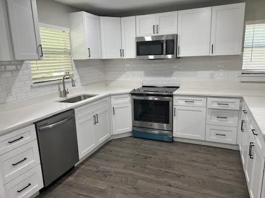 kitchen with white cabinets, appliances with stainless steel finishes, dark wood finished floors, and a sink