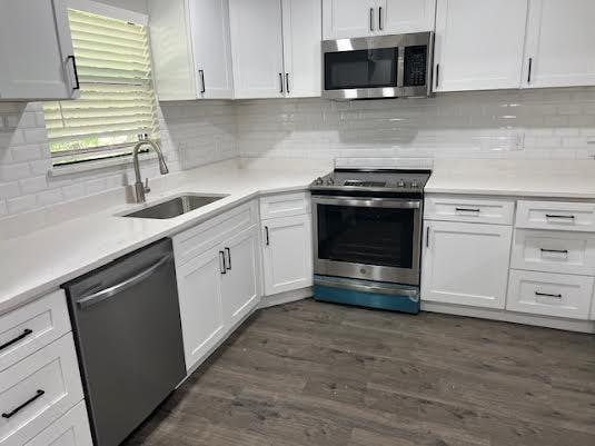 kitchen with white cabinets, dark wood-type flooring, stainless steel appliances, light countertops, and a sink