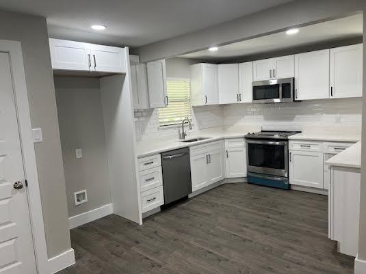 kitchen with tasteful backsplash, sink, white cabinets, dark hardwood / wood-style flooring, and stainless steel appliances