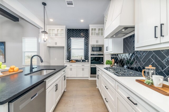 kitchen with sink, pendant lighting, white cabinets, custom range hood, and appliances with stainless steel finishes