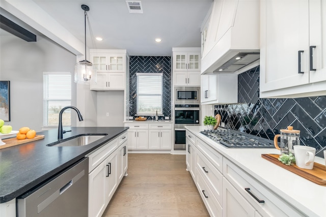 kitchen featuring premium range hood, sink, white cabinets, hanging light fixtures, and stainless steel appliances