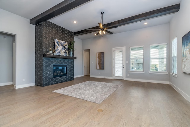 unfurnished living room featuring a tiled fireplace, ceiling fan, beamed ceiling, and light hardwood / wood-style floors