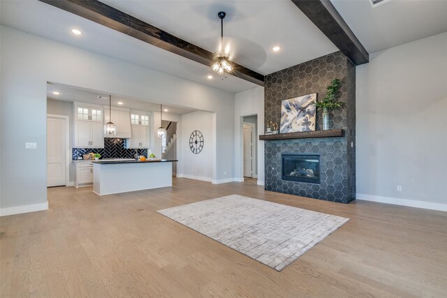 living room with a tile fireplace, beam ceiling, light hardwood / wood-style floors, and ceiling fan