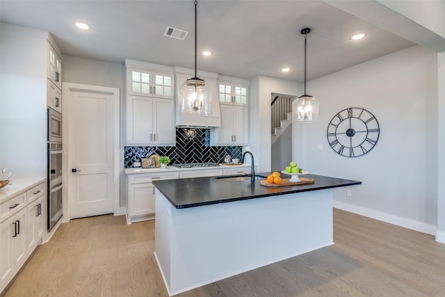 kitchen with stainless steel appliances, sink, pendant lighting, a center island with sink, and white cabinets