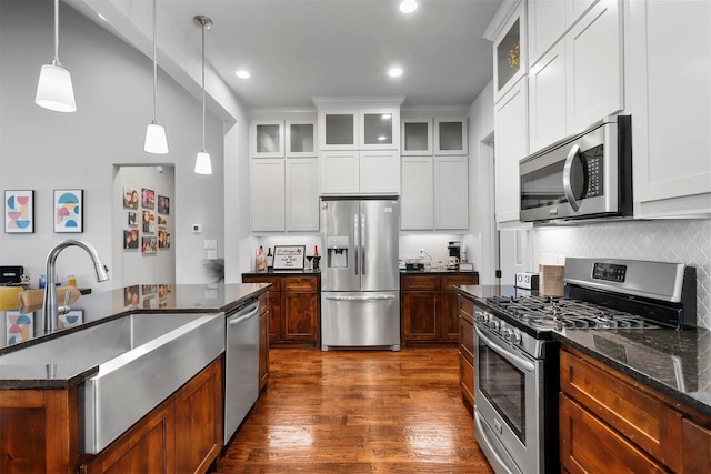 kitchen with decorative backsplash, appliances with stainless steel finishes, pendant lighting, dark stone countertops, and white cabinetry