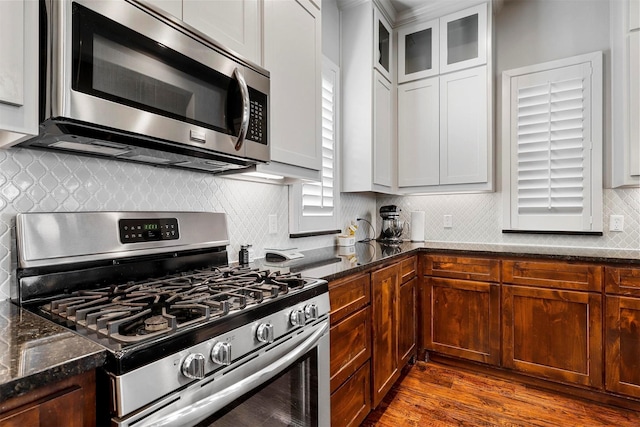 kitchen with stainless steel appliances, tasteful backsplash, dark hardwood / wood-style flooring, dark stone countertops, and white cabinets