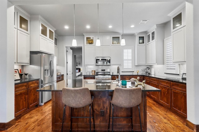 kitchen featuring a kitchen breakfast bar, stainless steel appliances, a kitchen island with sink, hardwood / wood-style flooring, and hanging light fixtures