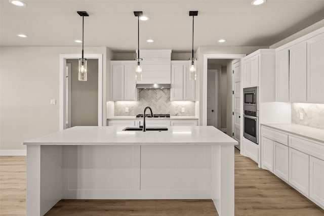 kitchen with light stone counters, a center island with sink, white cabinets, and appliances with stainless steel finishes